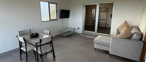 A spacious living area with a dining table, sofa, and a TV mounted on the wall.