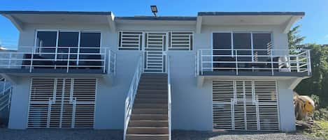 Un edificio de dos pisos con una escalera central, balcones y ventanas amplias.