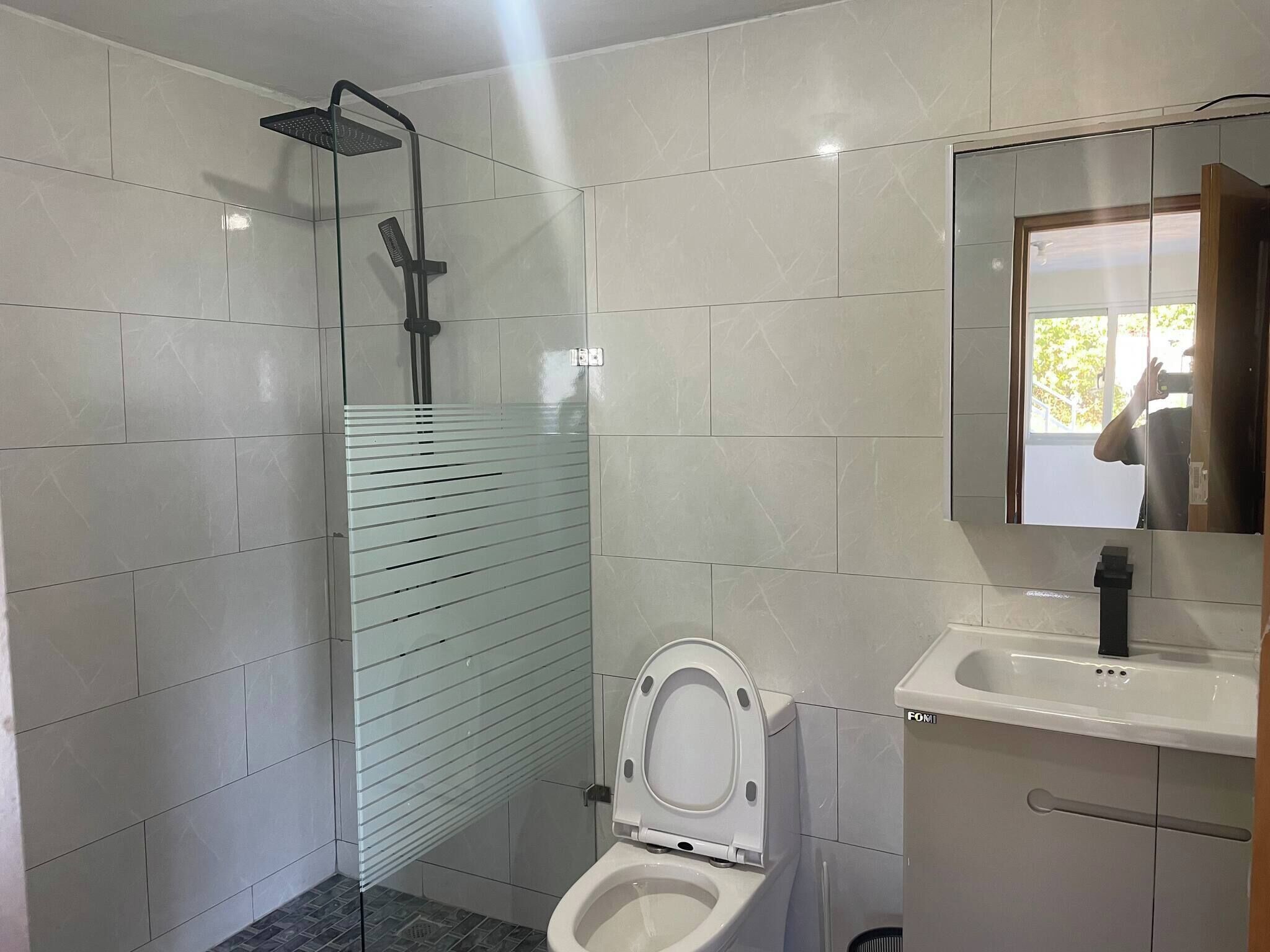 A bathroom with a glass shower enclosure, a toilet, and a sink with a mirror.