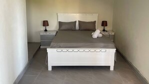Habitación de hotel estrecha con una cama individual, dos mesitas de noche y una mesita auxiliar.