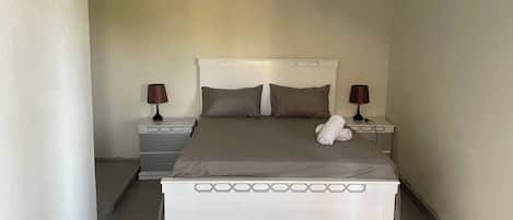 A narrow hotel room with a single bed, two bedside tables, and a nightstand.