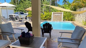 Zona junto a la piscina con sillones de descanso, una mesa y una cesta de objetos.