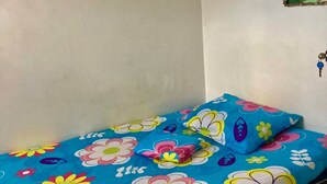 Een kleine kamer met een enkel bed en een kleurrijke bloemenprint sprei.