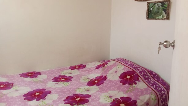 Een kamer met een bed dat is overdekt met een bloemenprint, een deur met een sleutelgat, en twee kleine foto's in lijsten aan de muur.