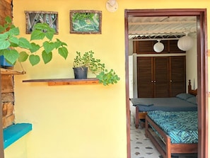 A room with a bed, a shelf with plants, and a wooden door. - Room-room Mirador, Casa Del Pueblo (Jardin)