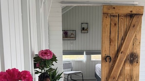 Una habitación con pared blanca, puerta de madera, una mesa blanca con planta en maceta y una silla.