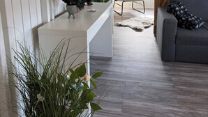 Una habitación con techo de madera blanca, un sofá gris, un mostrador blanco con plantas y paredes de madera.