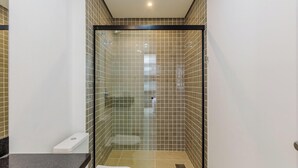 Une douche fermée par des parois en verre, avec un mur recouvert de carreaux, des toilettes et un lavabo.
