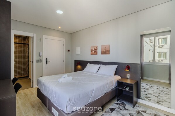 Quarto de hotel com cama, mesa de cabeceira e vista para o exterior.