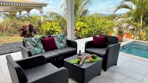 A patio area with wicker furniture, a pool, and tropical plants.