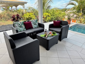 A patio area with wicker furniture, a pool, and tropical plants.