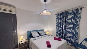 A bedroom with a bed, nightstands, a lamp, a blue chair, and a patterned curtain.