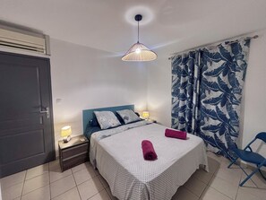 A bedroom with a bed, nightstands, a lamp, a blue chair, and a patterned curtain.