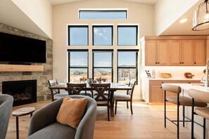 A modern living room with a fireplace, dining area, and kitchen with large windows. - Min to Deer Valley East Newest Terrain, Community Amenities, Free Ski Shuttle (Heber City)