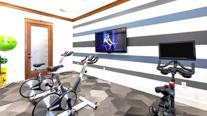 A room with two stationary bikes, a television mounted on the wall, and a door. - Stylish 1BR Resort Retreat Near The Woodlands (Conroe)