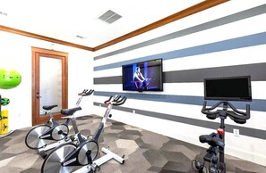 A room with two stationary bikes, a television mounted on the wall, and a door. - Stylish 1BR Resort Retreat Near The Woodlands (Conroe)