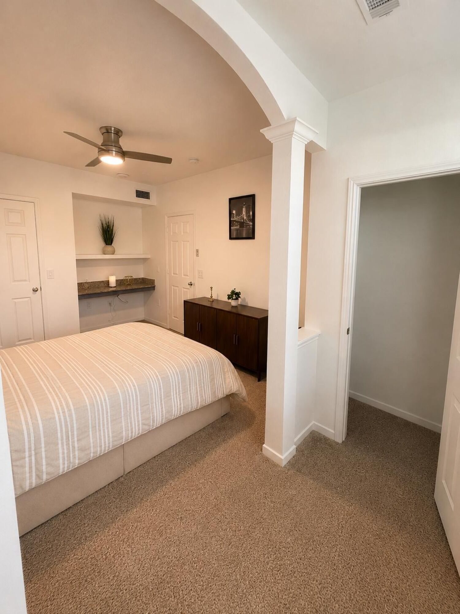 A bedroom with a bed, a ceiling fan, a dresser, and a closet.