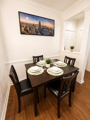 A dining room with a dark wooden table set for four, white plates, and green placemats. - Stylish 1BR Resort Retreat Near The Woodlands (Conroe)