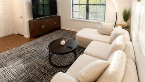 A modern living room with a sectional sofa, a flat-screen TV, and a patterned rug. - Stylish 1BR Resort Retreat Near The Woodlands (Conroe)