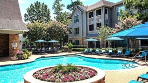 A swimming pool with lounge chairs and umbrellas, surrounded by a brick patio and a building with balconies. - Stylish 1BR Resort Retreat Near The Woodlands (Conroe)