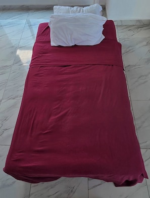 A single bed with a red bedspread and white pillows in a room with marble flooring.