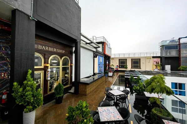 Un salón de barbería con suelo de madera y zona de estar exterior con mesas y sillas.