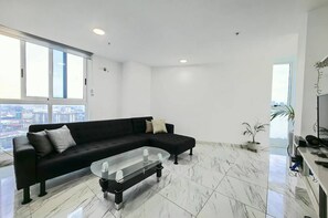 Una sala de estar moderna con un sofá seccional negro, una mesa de centro de vidrio y vistas a la ciudad a través de grandes ventanales.