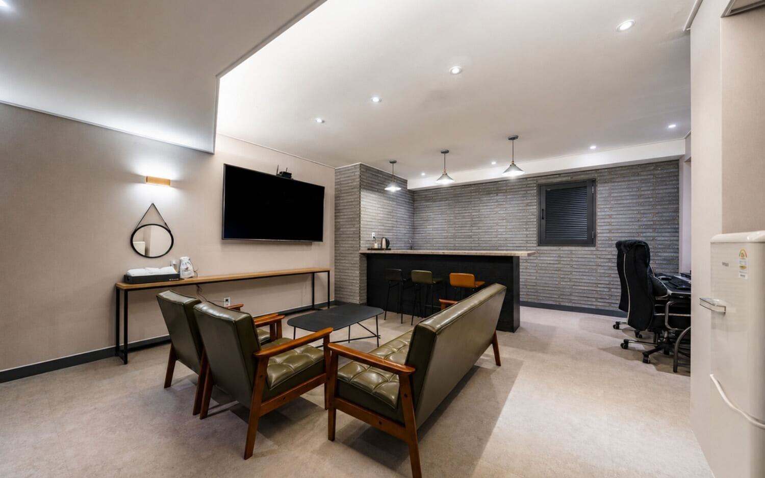 A modern hotel room with a dining area, a flat-screen TV, a kitchen counter, and a seating area with chairs.