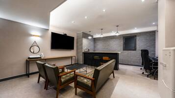 A modern hotel room with a dining area, a flat-screen TV, a kitchen counter, and a seating area with chairs.