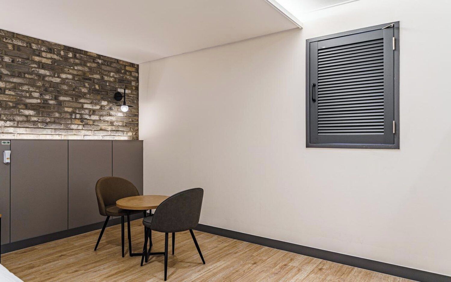 A small room with a brick wall, a window with blinds, and two chairs.