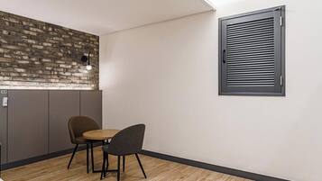 A small room with a brick wall, a window with blinds, and two chairs.