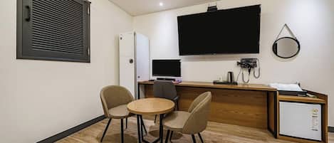 Habitación de hotel compacta con kitchenette, un televisor de pantalla plana en la pared, un refrigerador pequeño, un escritorio con computadora y dos sillas alrededor de una mesita redonda.