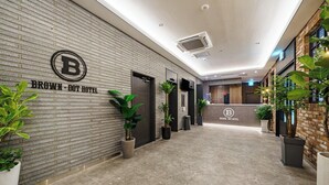 Zona de recepción de un hotel con diseño moderno, que presenta una pared de ladrillo, un mostrador de recepción y plantas en macetas.