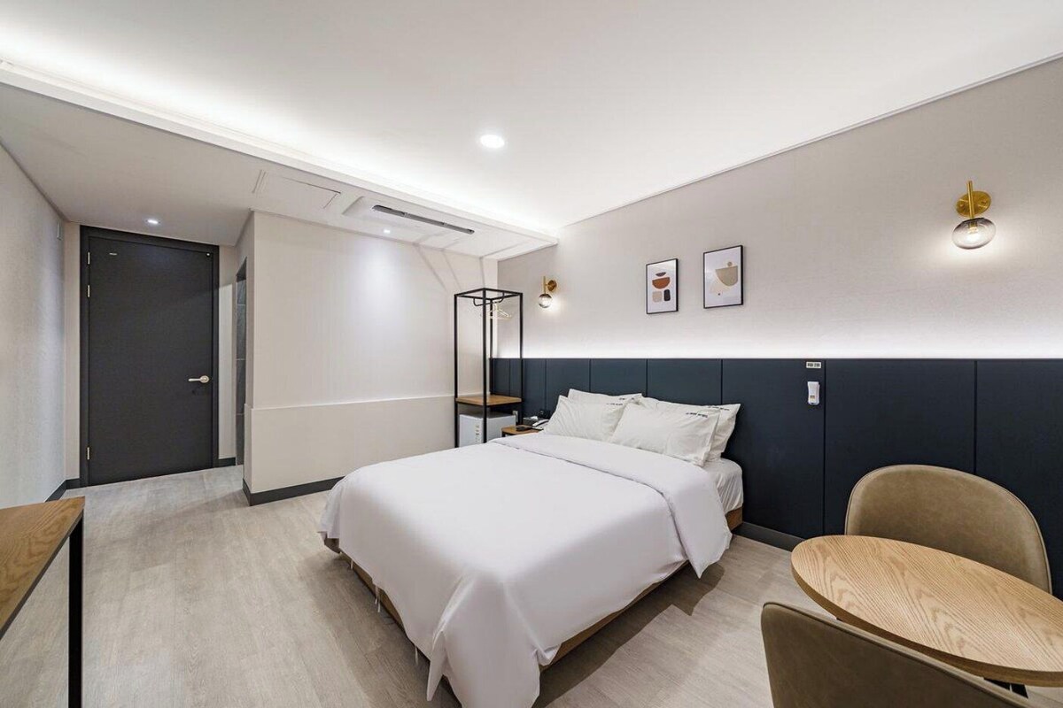 A modern hotel room with a bed, bedside table, chair, and a small round table.