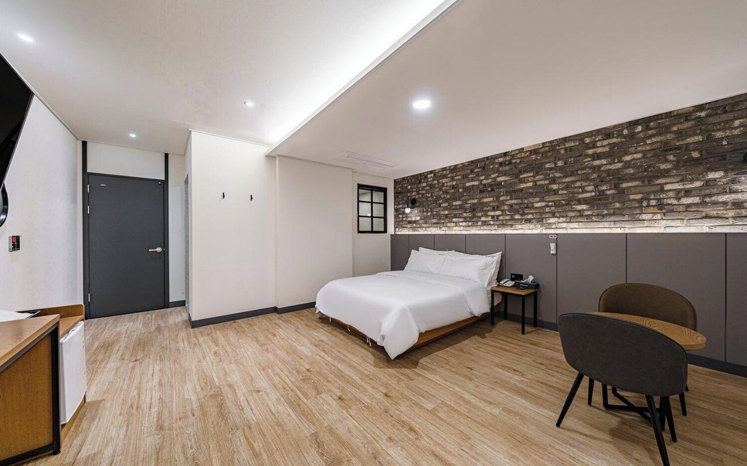 A modern hotel room with a bed, a desk, a chair, and a brick-patterned wall.