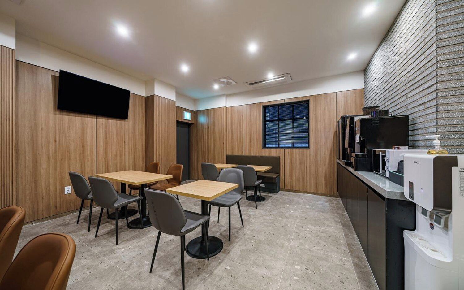 A modern interior with wooden panel walls, a flat-screen TV mounted on the wall, and a counter with a coffee machine.