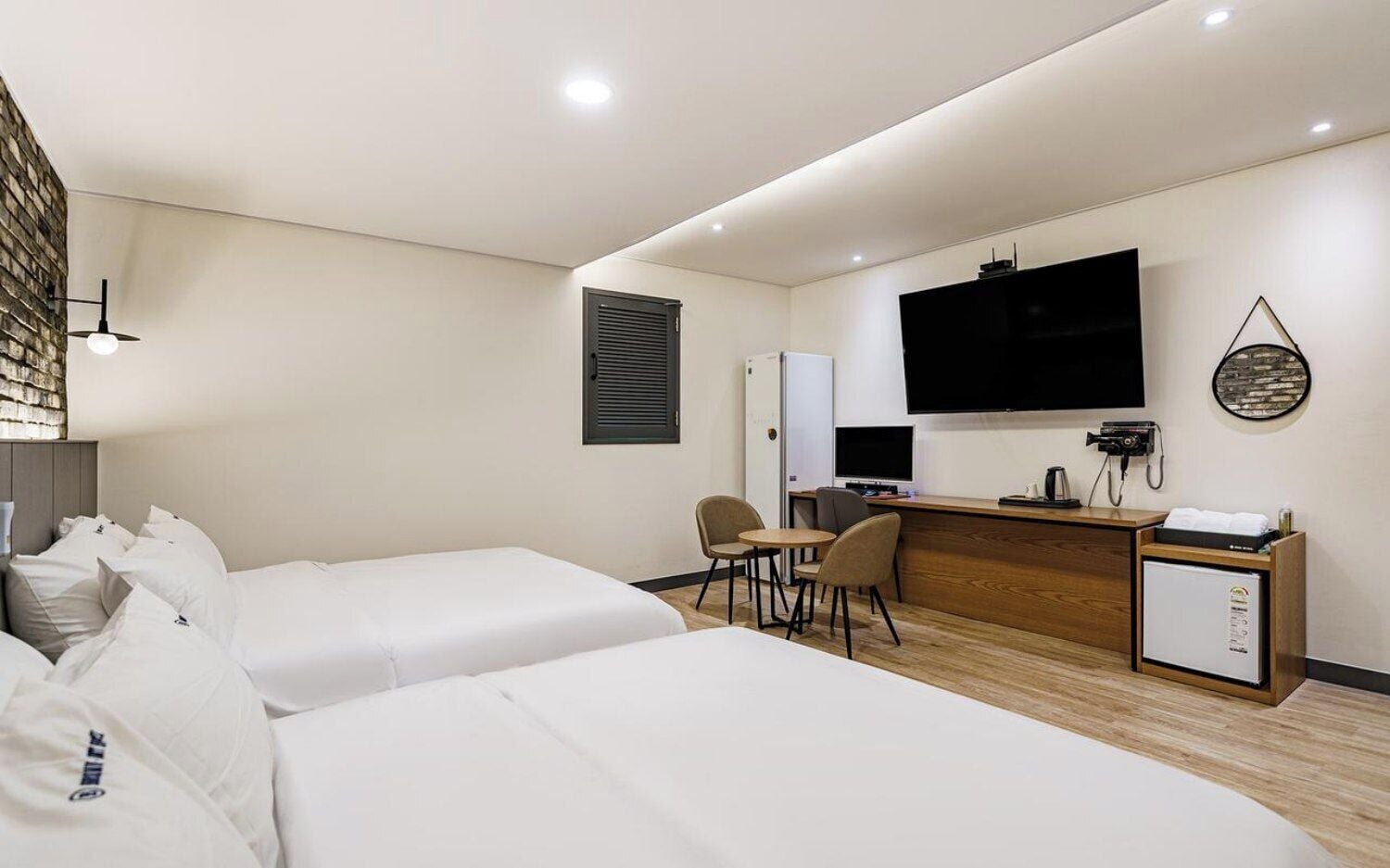 A hotel room with two beds, a desk with a computer, a TV, and a minibar.