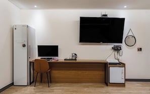 Habitación de hotel con escritorio de madera, televisor montado en la pared, refrigerador y un pequeño mueble.