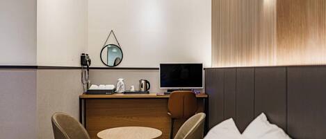 Habitación de hotel con cama, dos sillas, una mesita redonda, un escritorio con computadora, un espejo y una lámpara de pared.