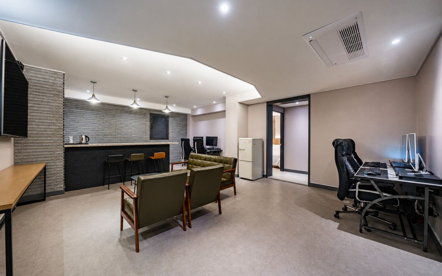 A modern hotel room with a kitchenette, seating area, and a desk with computers.
