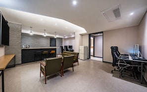 A modern hotel room with a kitchenette, seating area, and a desk with computers.