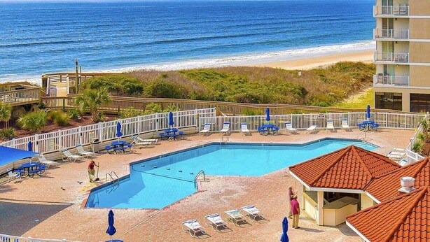 Ein Poolbereich mit Blick auf den Ozean, einen Strand und ein Gebäude mit Balkonen.