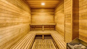 Eine Sauna mit Holzwänden und -bänken, einem geneigten Boden und einem sichtbaren Heizaggregat.