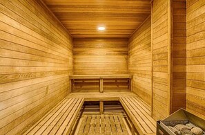 Eine Sauna mit Holzwänden und -bänken, einem geneigten Boden und einem sichtbaren Heizaggregat.