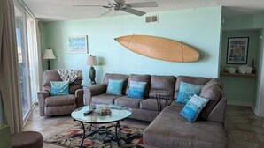 Ein Wohnzimmer mit einer Eckcouch, einem Couchtisch und einem Surfbrett an der Wand.