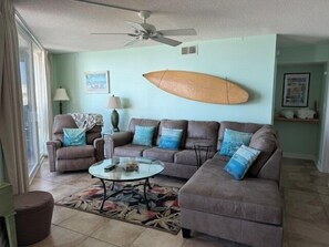 Ein Wohnzimmer mit einer Eckcouch, einem Couchtisch und einem Surfbrett an der Wand.
