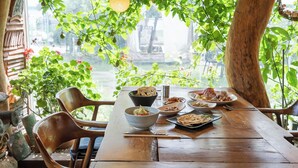 An outdoor dining area with a wooden table and chairs, surrounded by greenery and a view of a building. - Gyeongju Hanok Stay Damso (Gyeongju)
