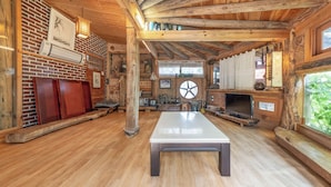 A rustic interior with a central table, wooden beams, brick walls, and a fireplace. - Gyeongju Hanok Stay Damso (Gyeongju)