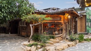 A rustic building with a traditional design, featuring a stone-paved entrance and a small garden area with rocks and plants. - Gyeongju Hanok Stay Damso (Gyeongju)