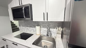 Una cucina moderna con mobili bianchi, un lavello in acciaio inossidabile, un forno a microonde e un forno integrato.